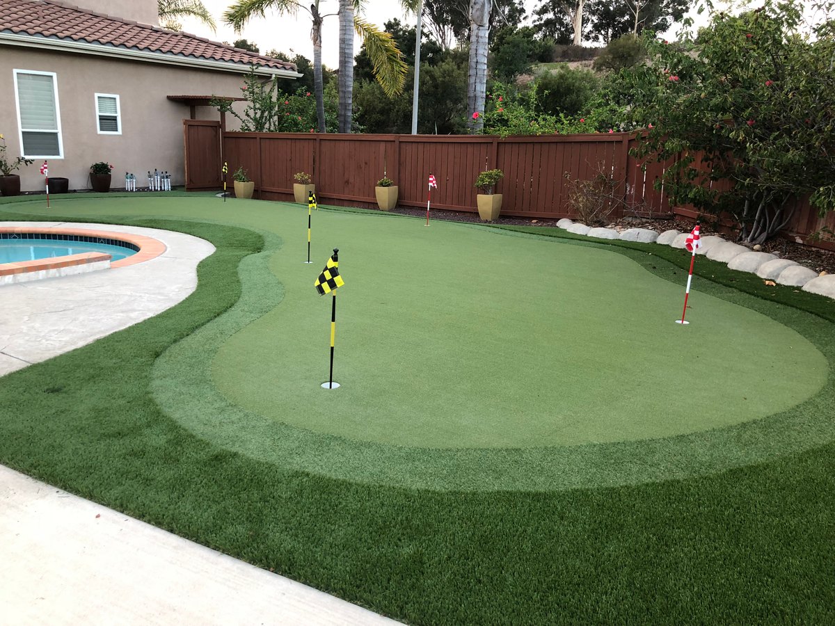 Backyard putting green with flags beside a pool by Panjia Outdoors