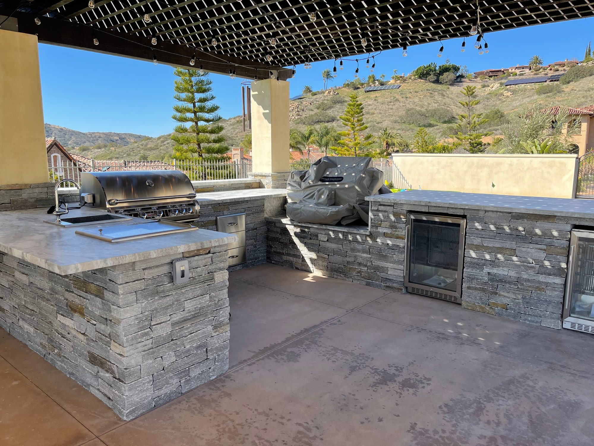 Custom stacked-stone outdoor kitchen with built-in grill, side burner, and hillside view by Panjia Outdoors in San Diego County